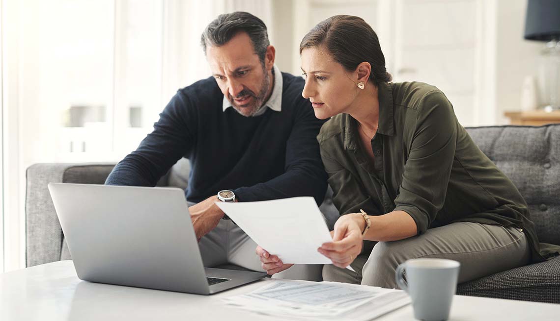 Couple discussing documents on laptop.